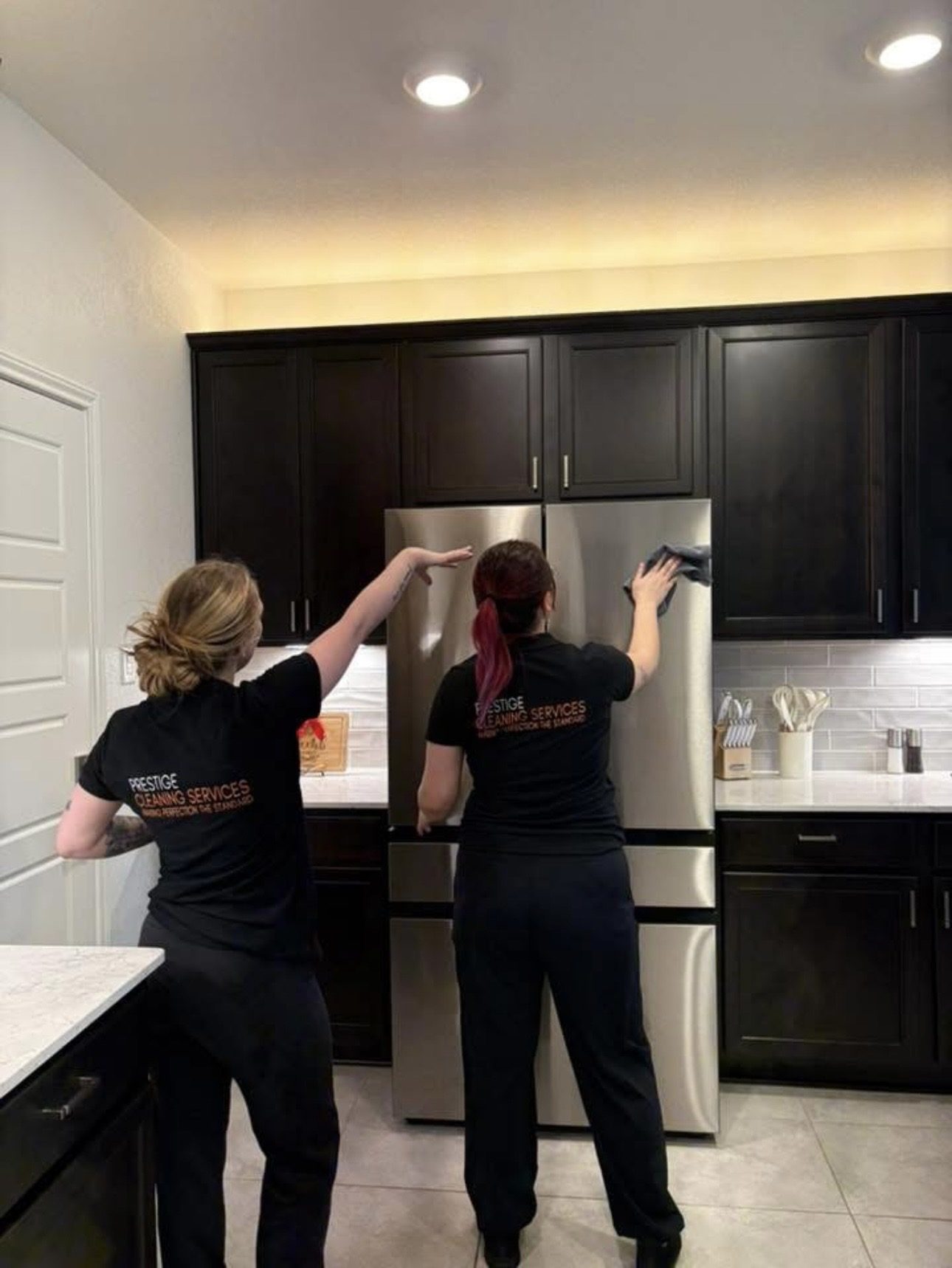 Prestige Cleaning Services team members cleaning a kitchen refrigerator
